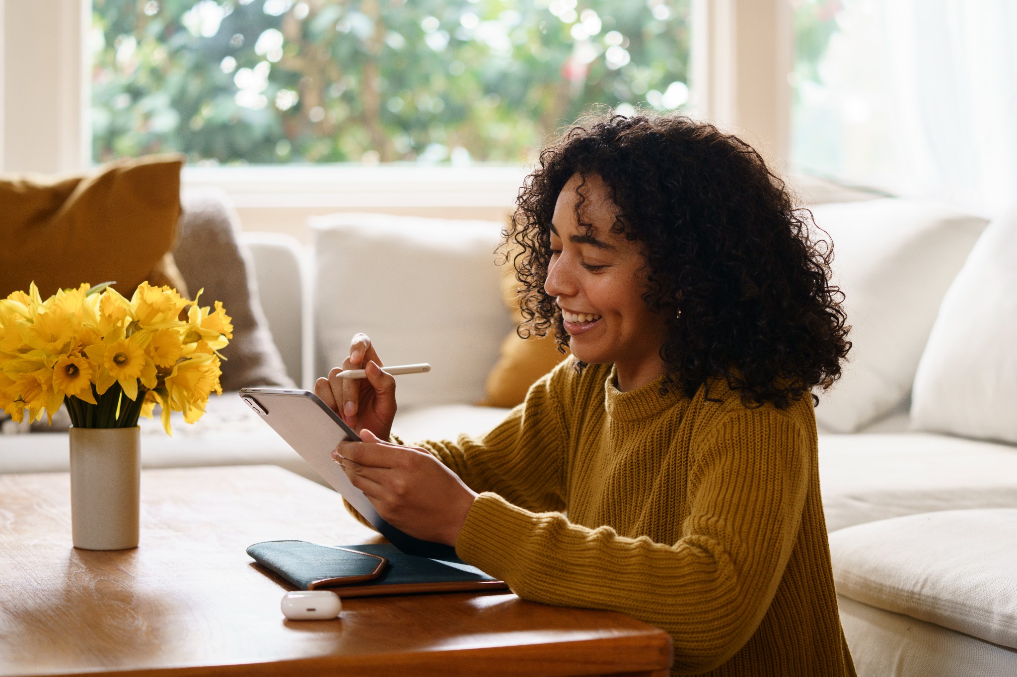 A smiling woman making plans with her tablet at a bright kitchen table.